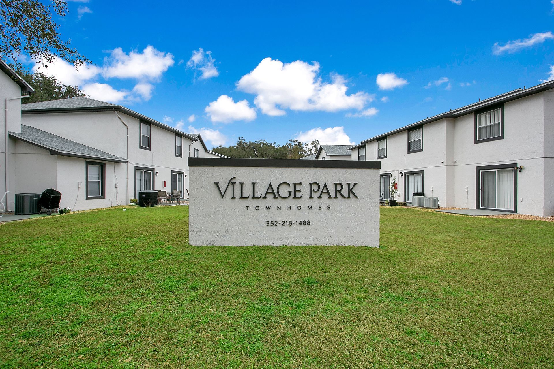 A sign for village park is in the middle of a lush green field.