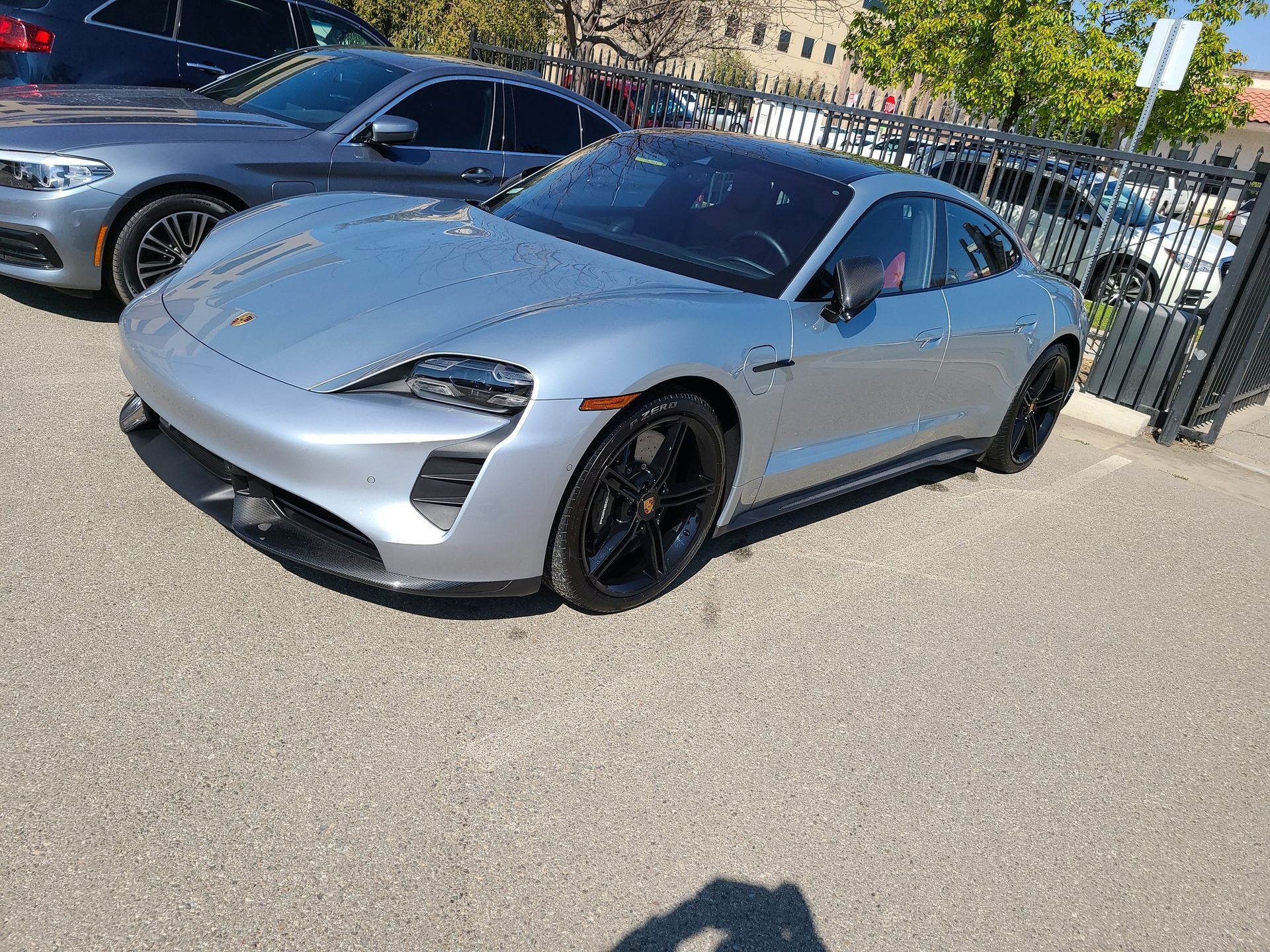 A silver porsche taycan is parked in a parking lot next to a bmw 5 series.