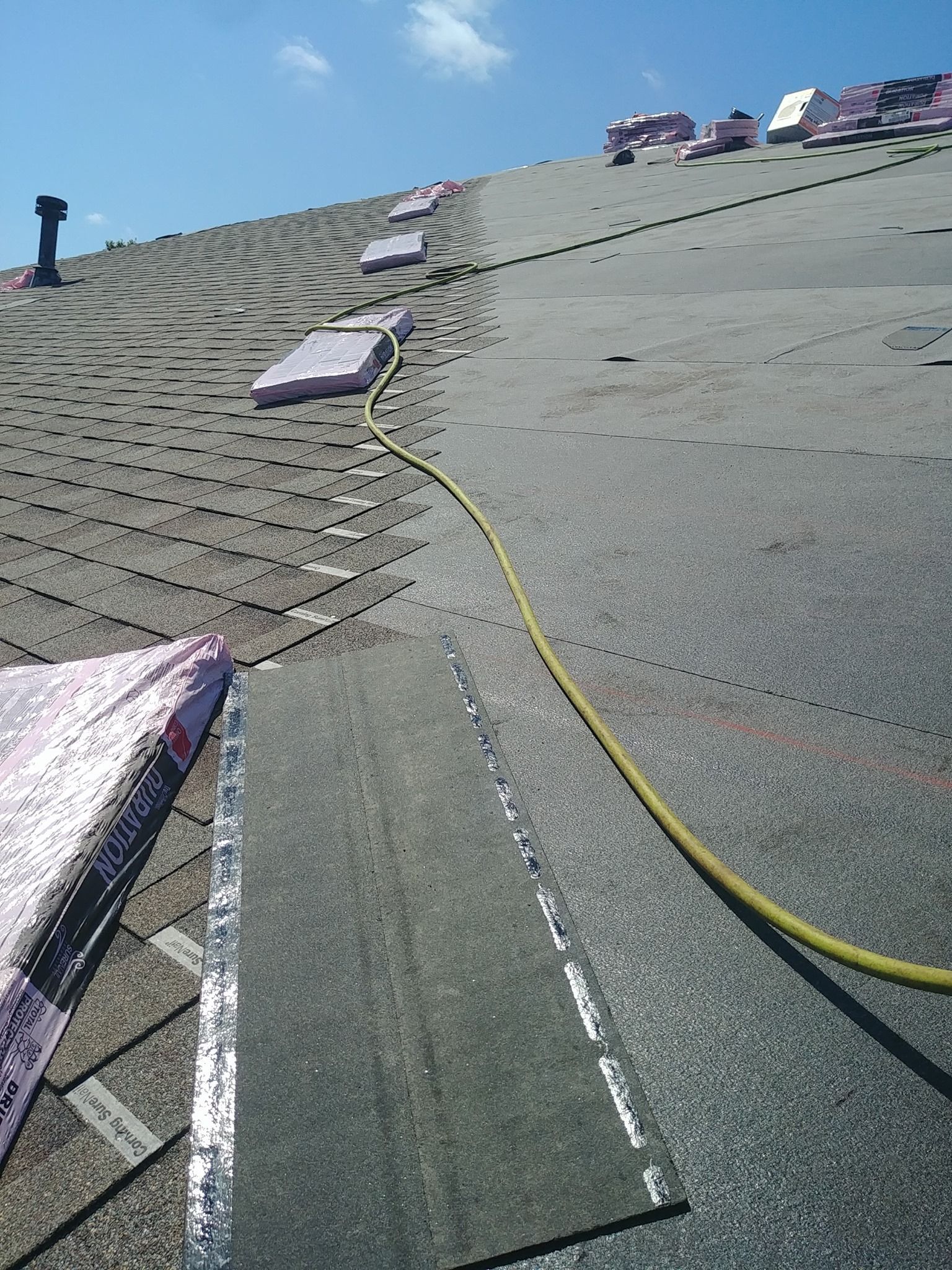 A man is sitting on the roof of a house installing asphalt roof.