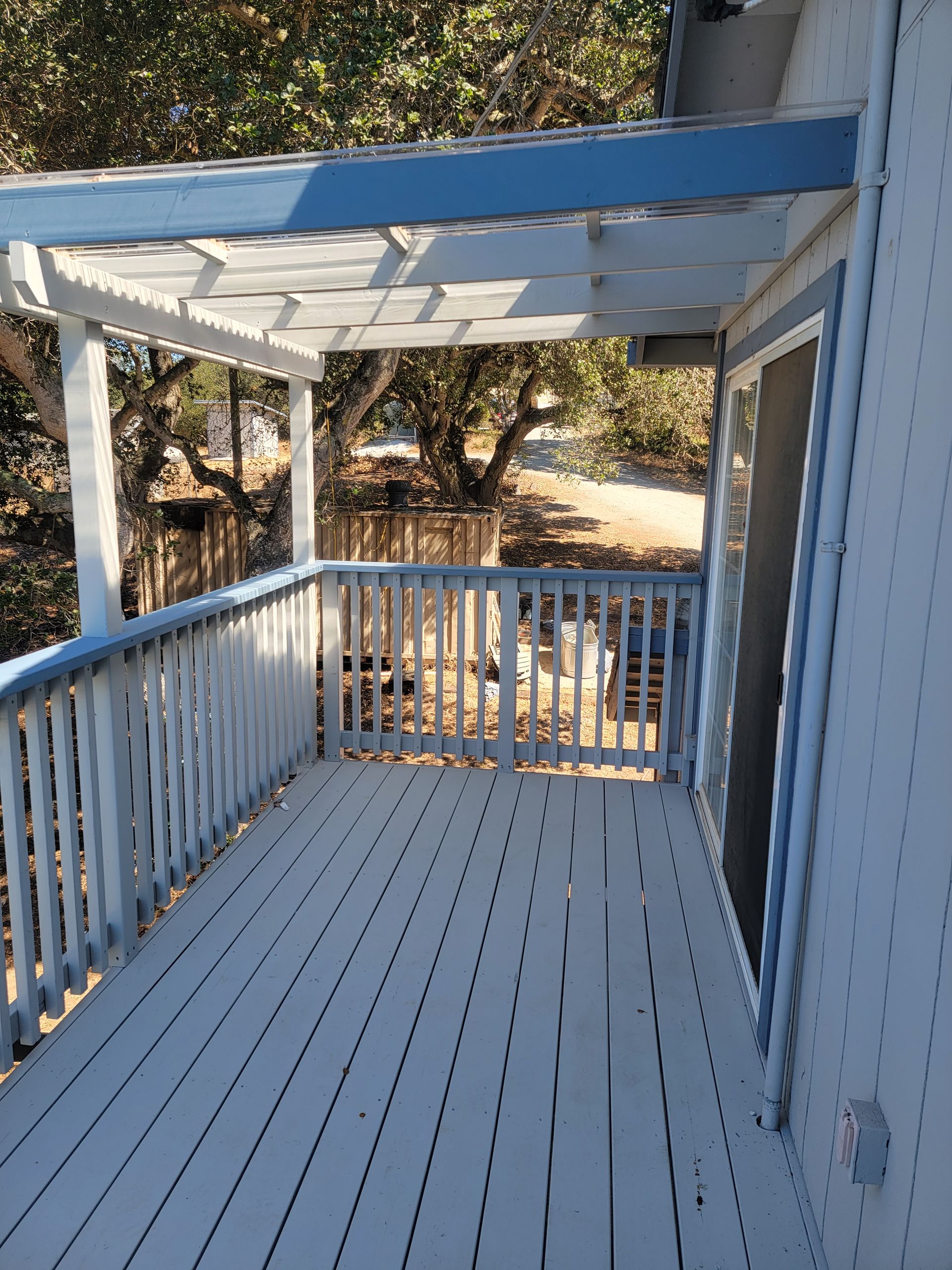 Deck with white and blue paint, pergola, overlooking a wooded yard.