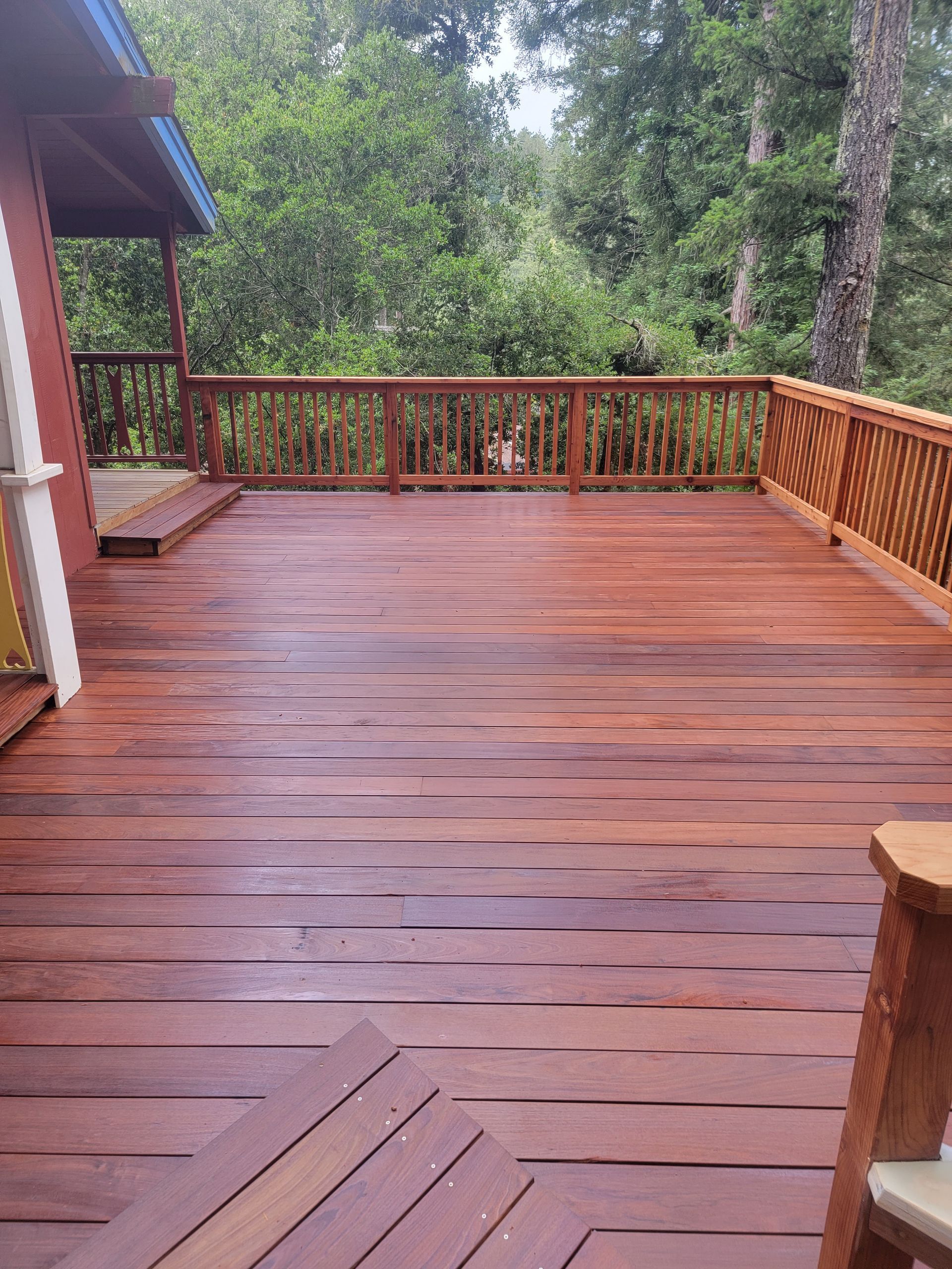 Wooden deck with railing, stained red-brown, overlooking a green forest.
