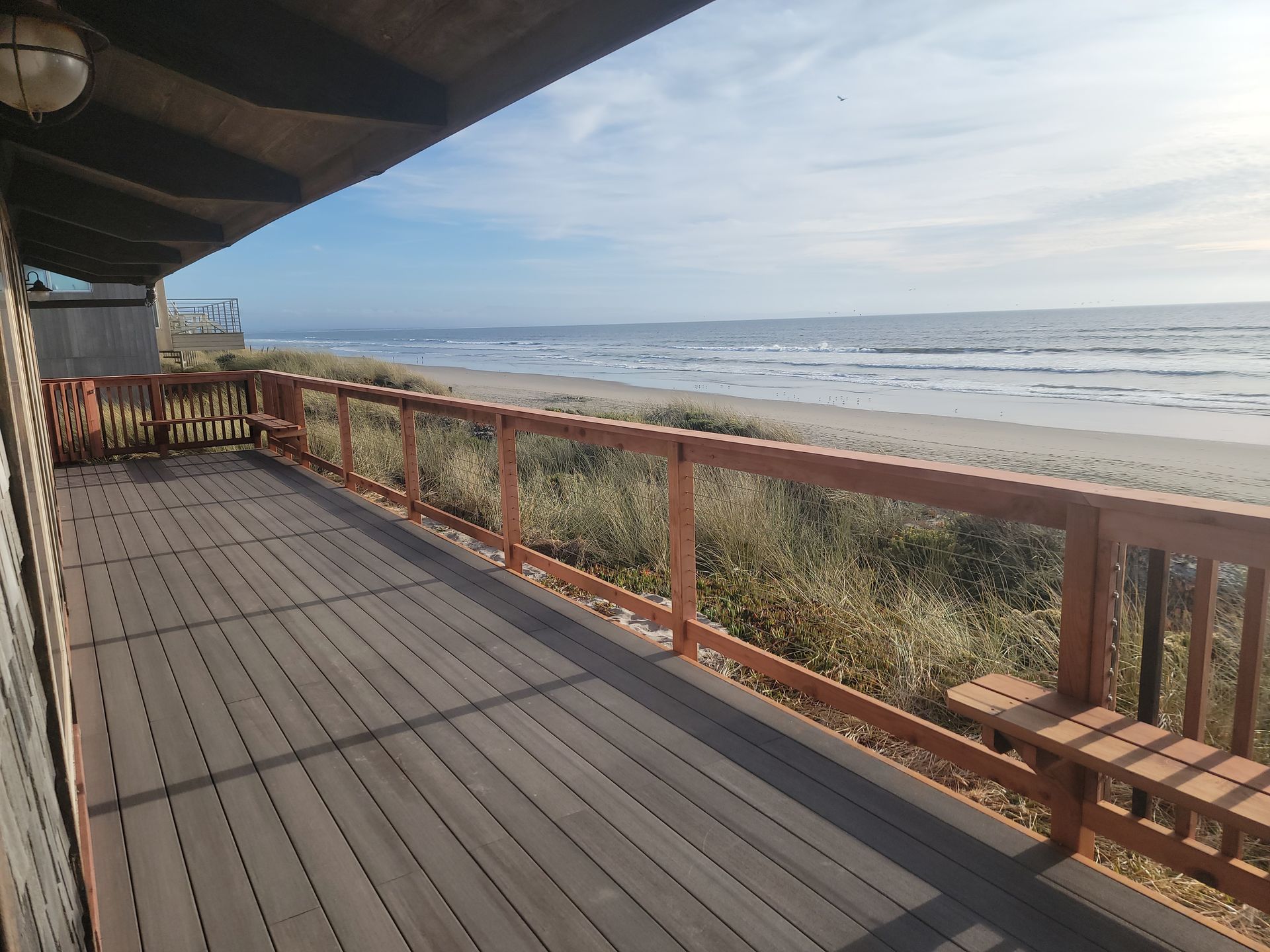 Wooden deck overlooking a sandy beach and ocean. Brown railing, cloudy sky.