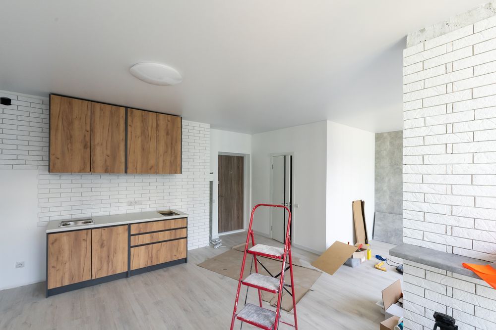 Kitchen under renovation with light-colored cabinets, white brick walls, and a red ladder.