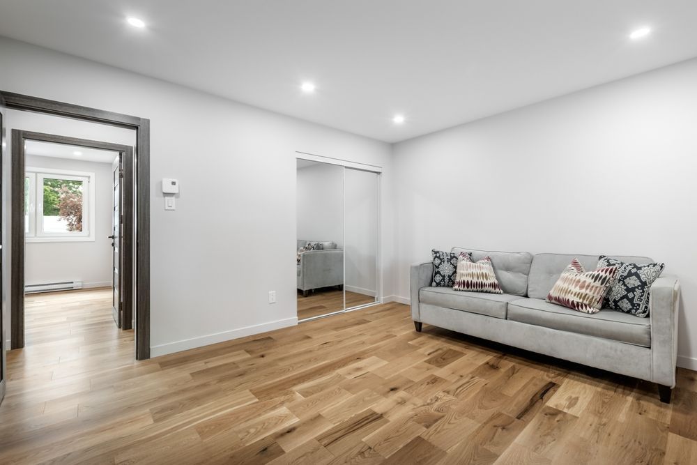 Empty living room with wood floor, gray sofa, and two doorways.