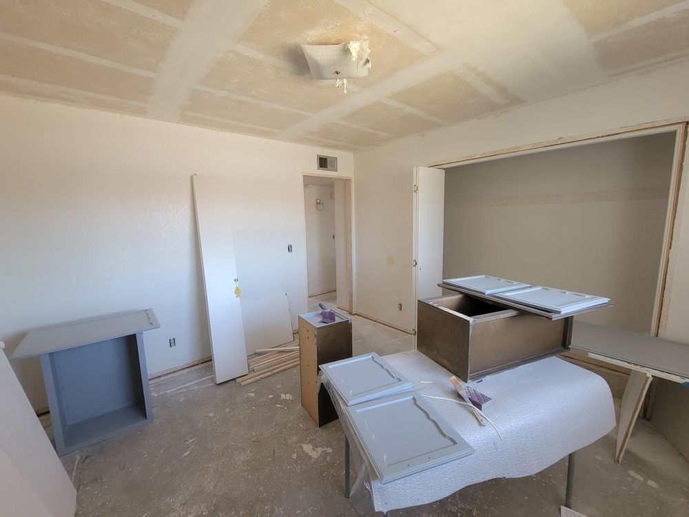 Room under construction with unfinished walls and ceiling; cabinet doors on a covered table.