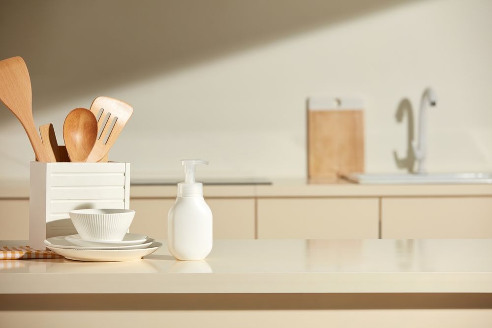 Kitchen counter with utensils, soap dispenser, dishes, and sink in soft light.