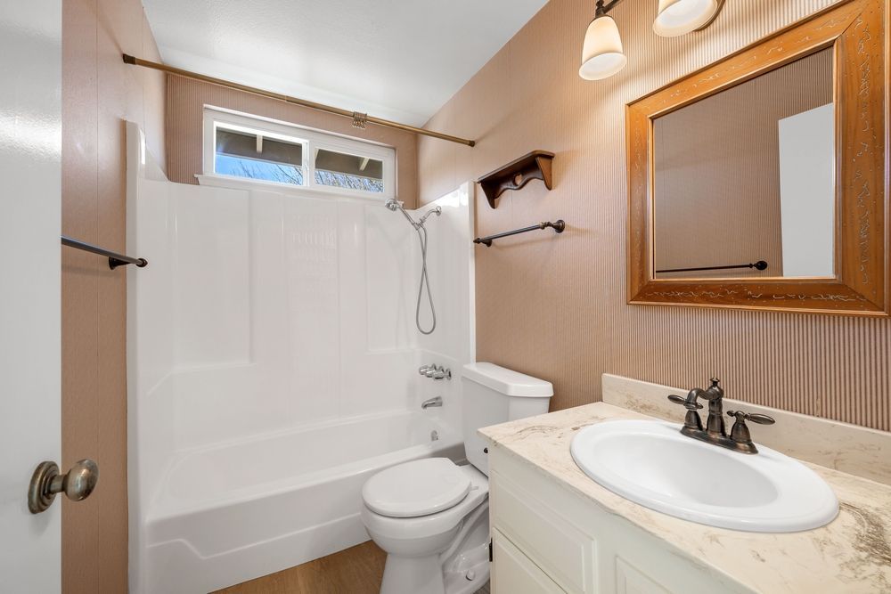 Bathroom with white tub, toilet, and vanity, tan walls, and a window.