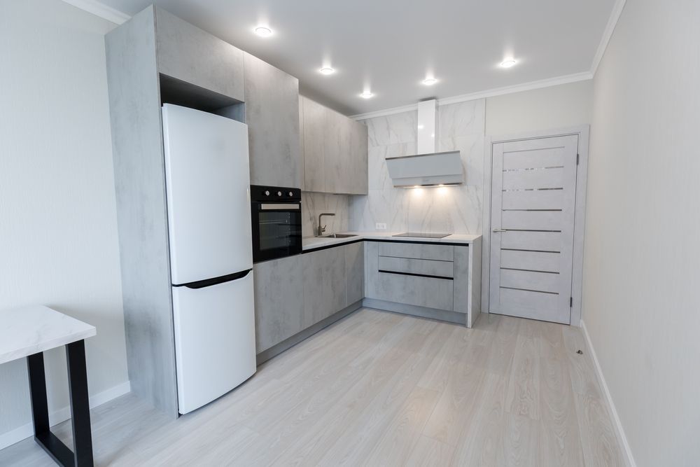 Modern gray kitchen with refrigerator, cabinets, oven, range hood, and door.