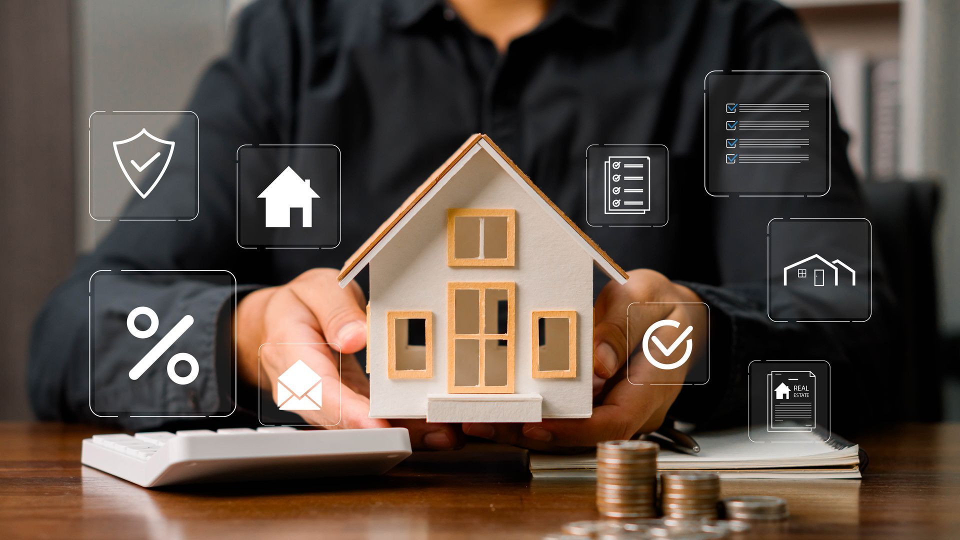 Person holding a model house with financial and real estate icons; calculator and coins on table.