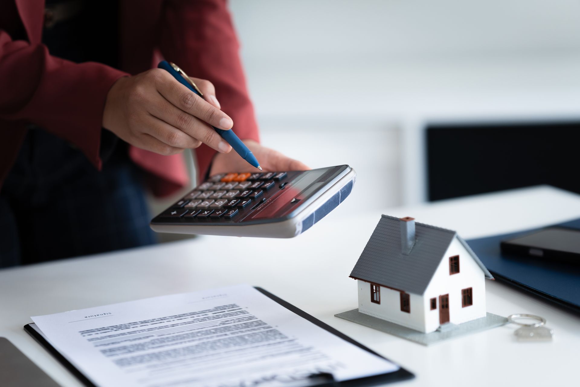 Person calculating on a calculator next to a model house and documents.