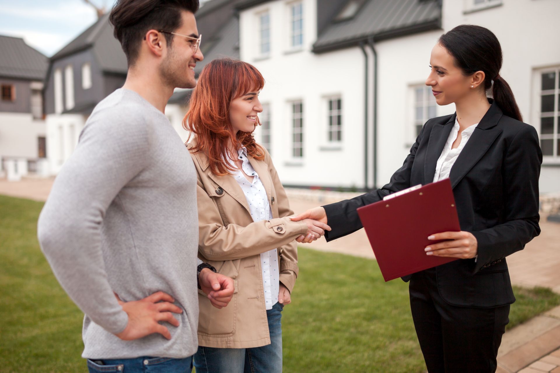 Real estate agent shaking hands with a couple in front of houses.