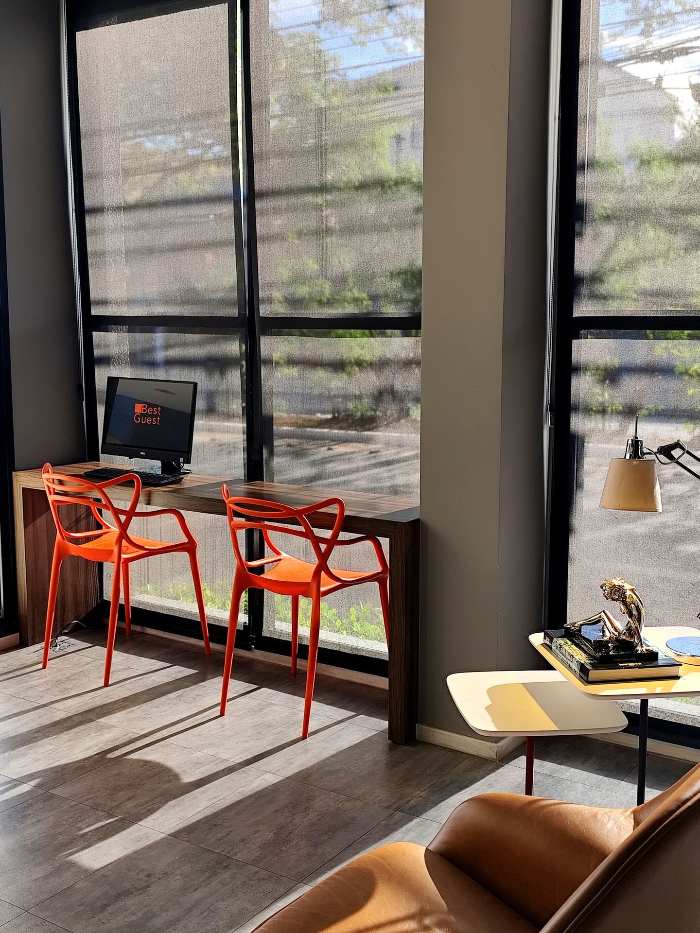 Escritório bem iluminado com mesa, cadeiras laranja e janela.