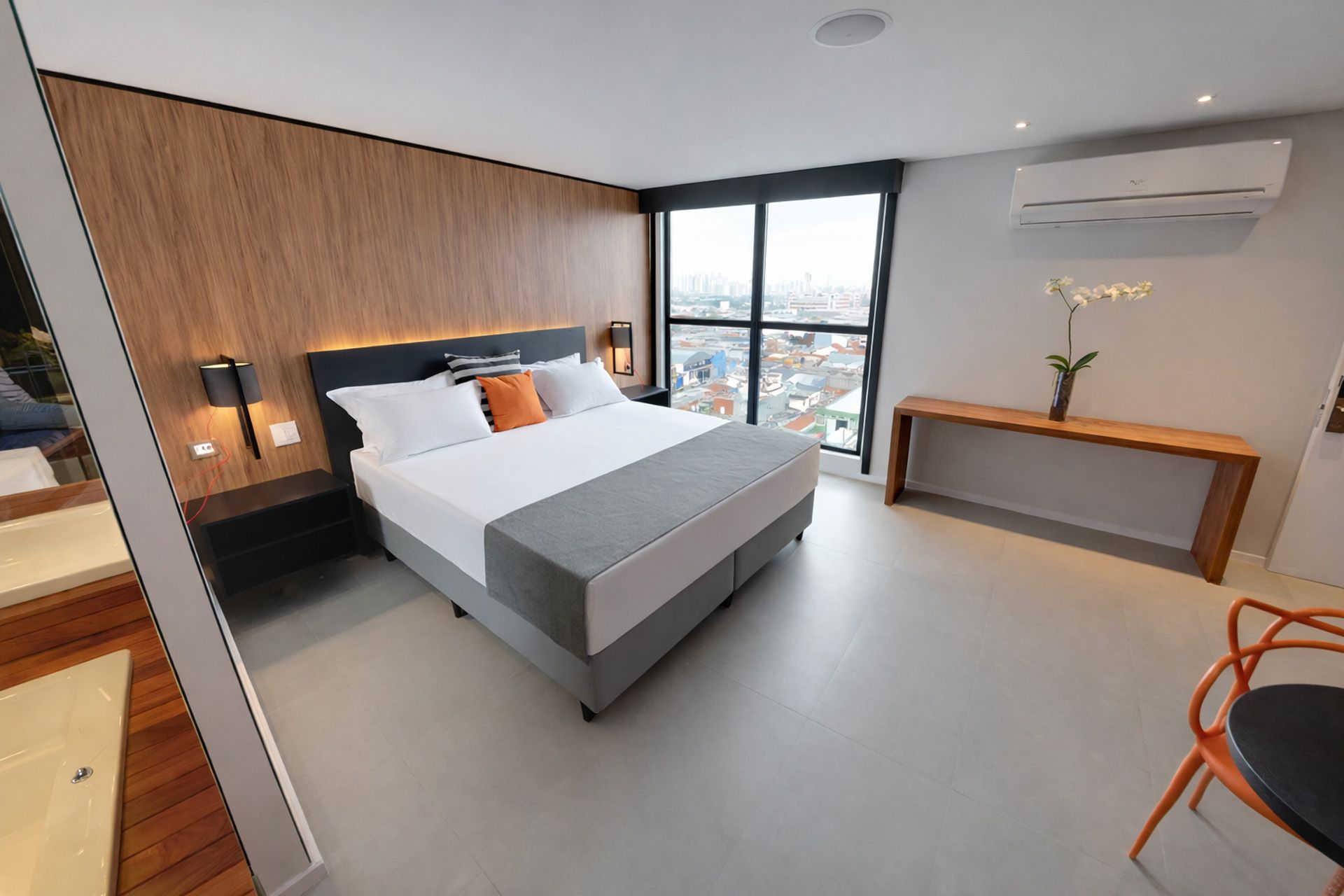 Quarto de hotel moderno com cama, painéis de madeira, uma grande janela e uma pequena mesa.