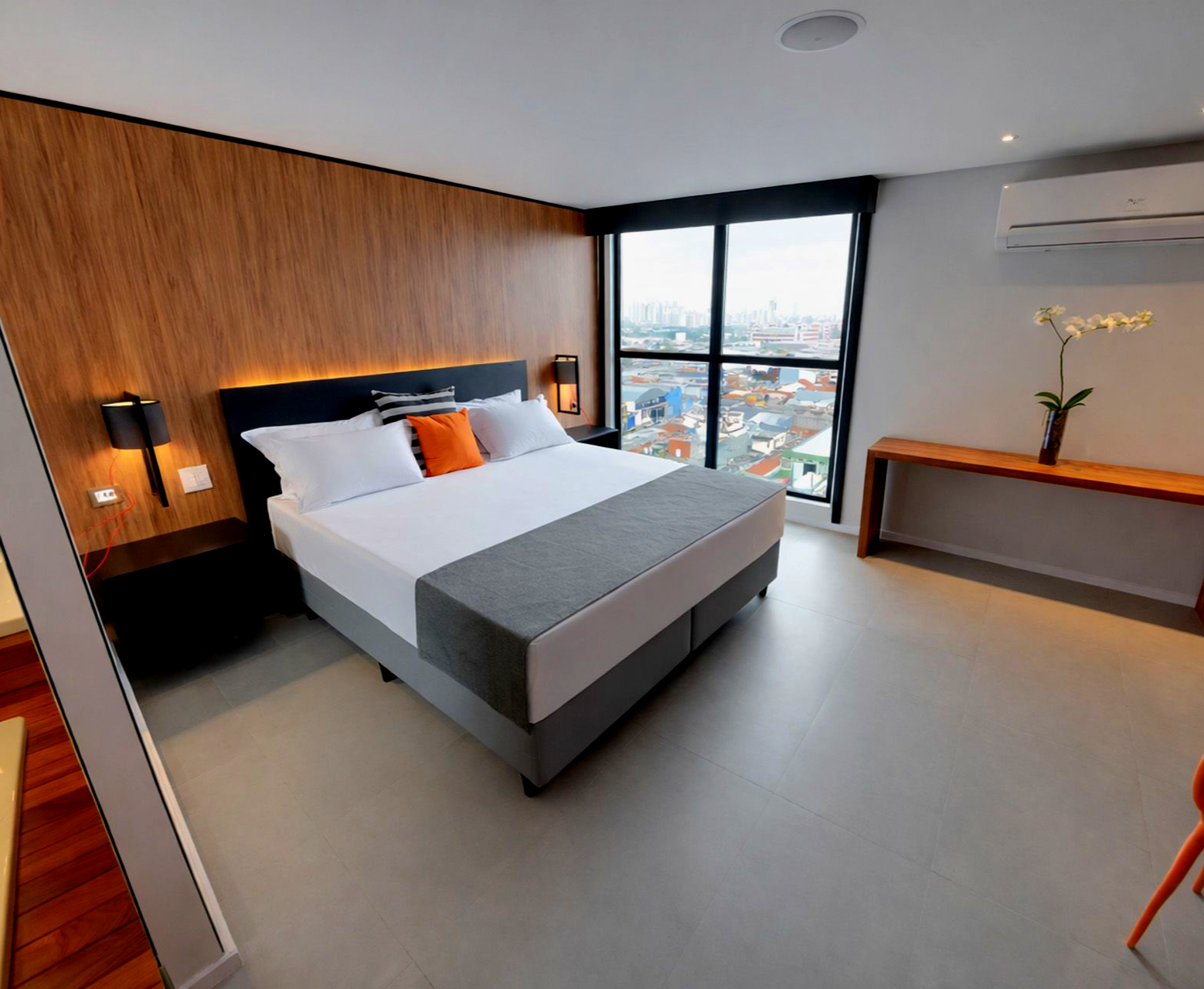 Quarto de hotel moderno com cama, painéis de madeira, uma grande janela e uma pequena mesa.