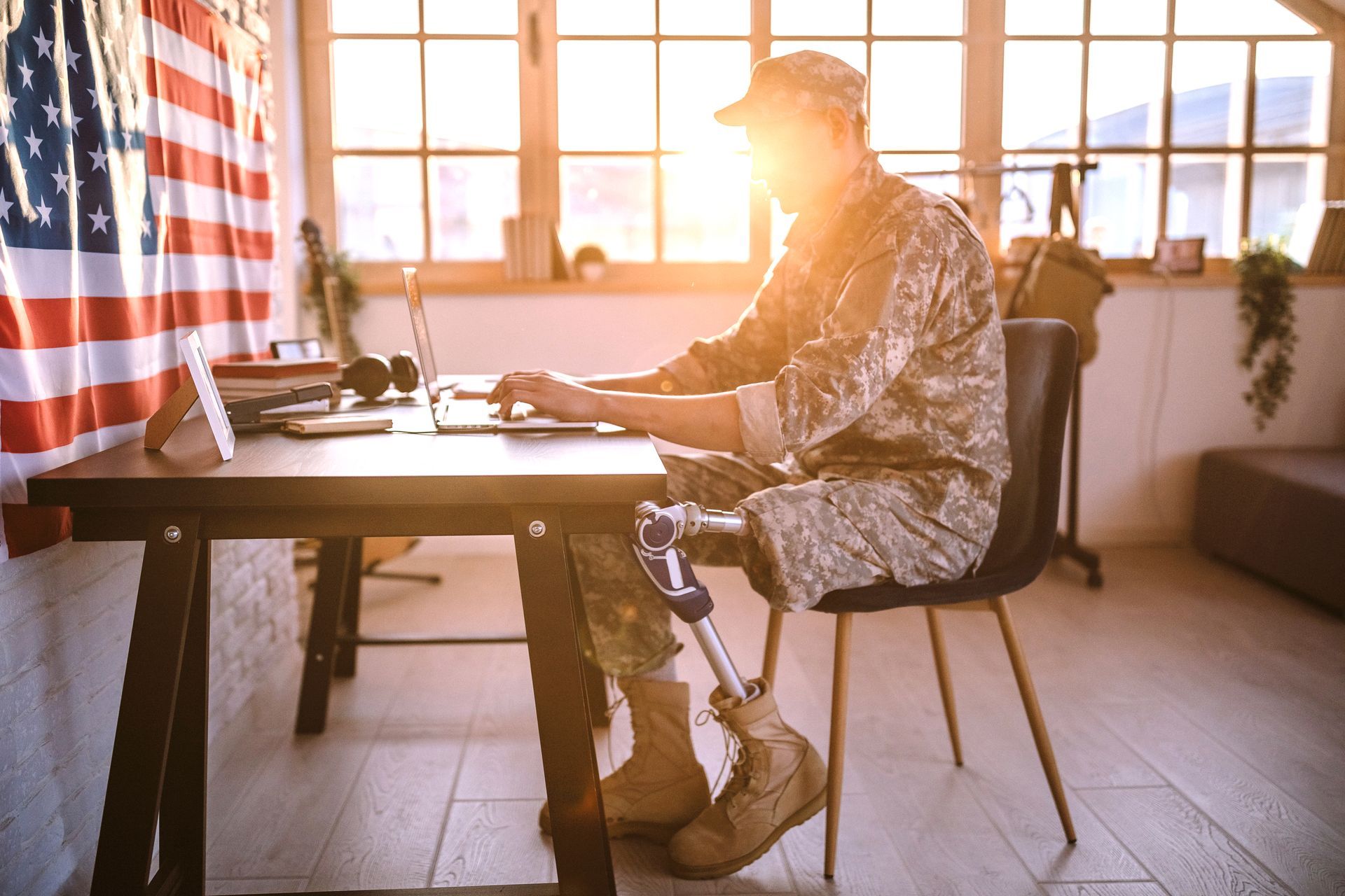A soldier with a prosthetic leg is sitting at a desk using a laptop computer.