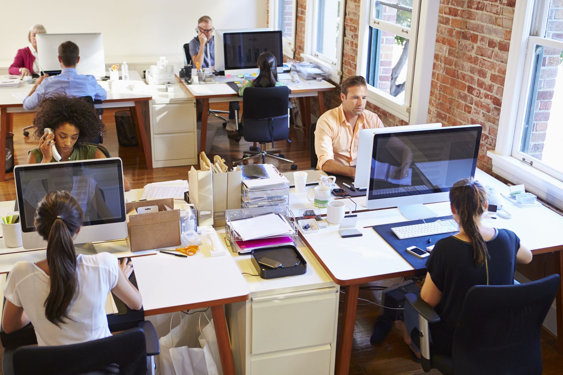 A group of people are sitting at desks in an office working on computers.