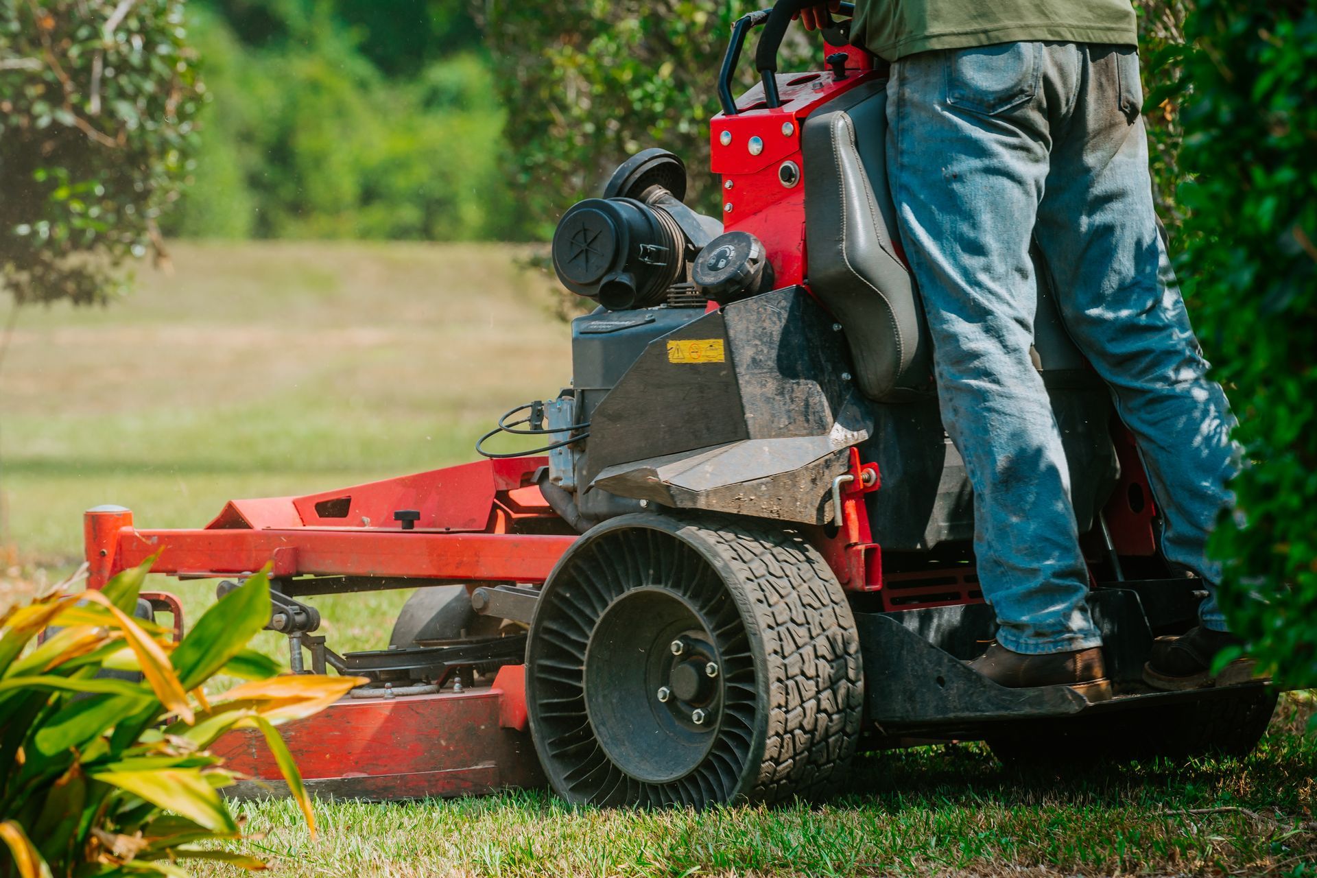 A person operating a red lawn mower on a grassy lawn