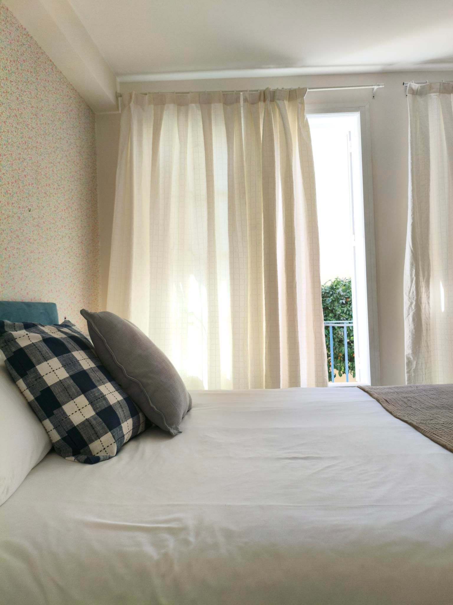 Bedroom with white bed, patterned pillows, and sheer curtains over a balcony.
