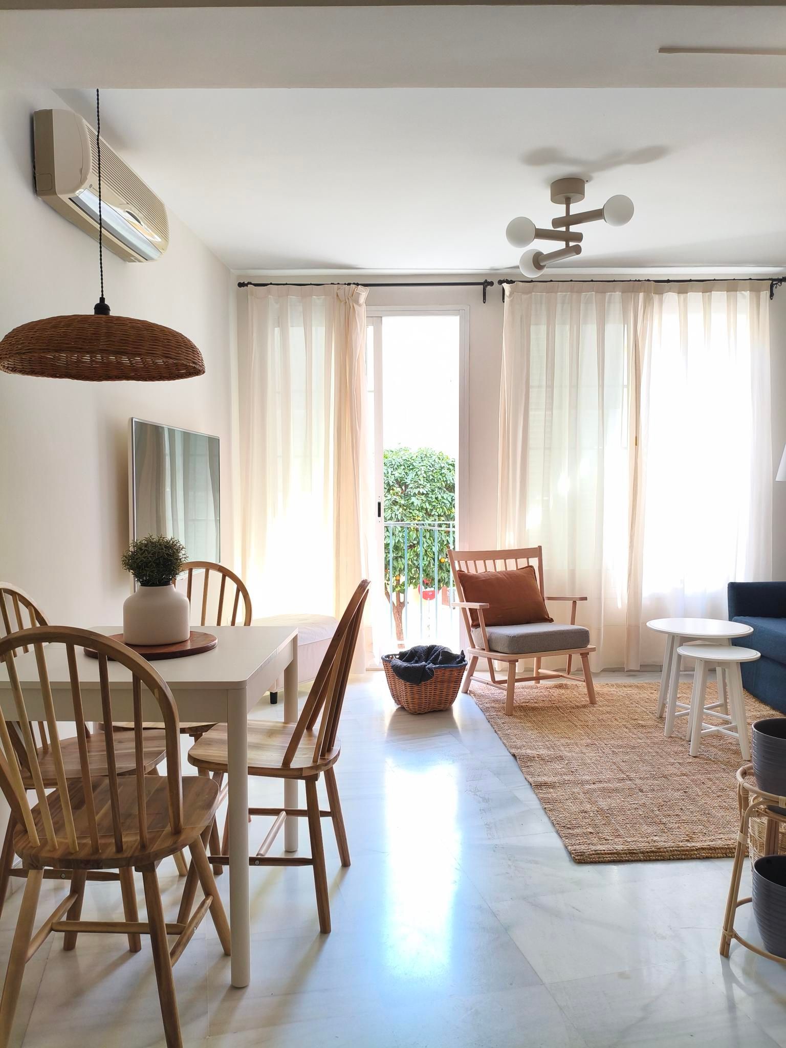 Living room with a dining table, chairs, and a seating area near a balcony with sheer curtains.