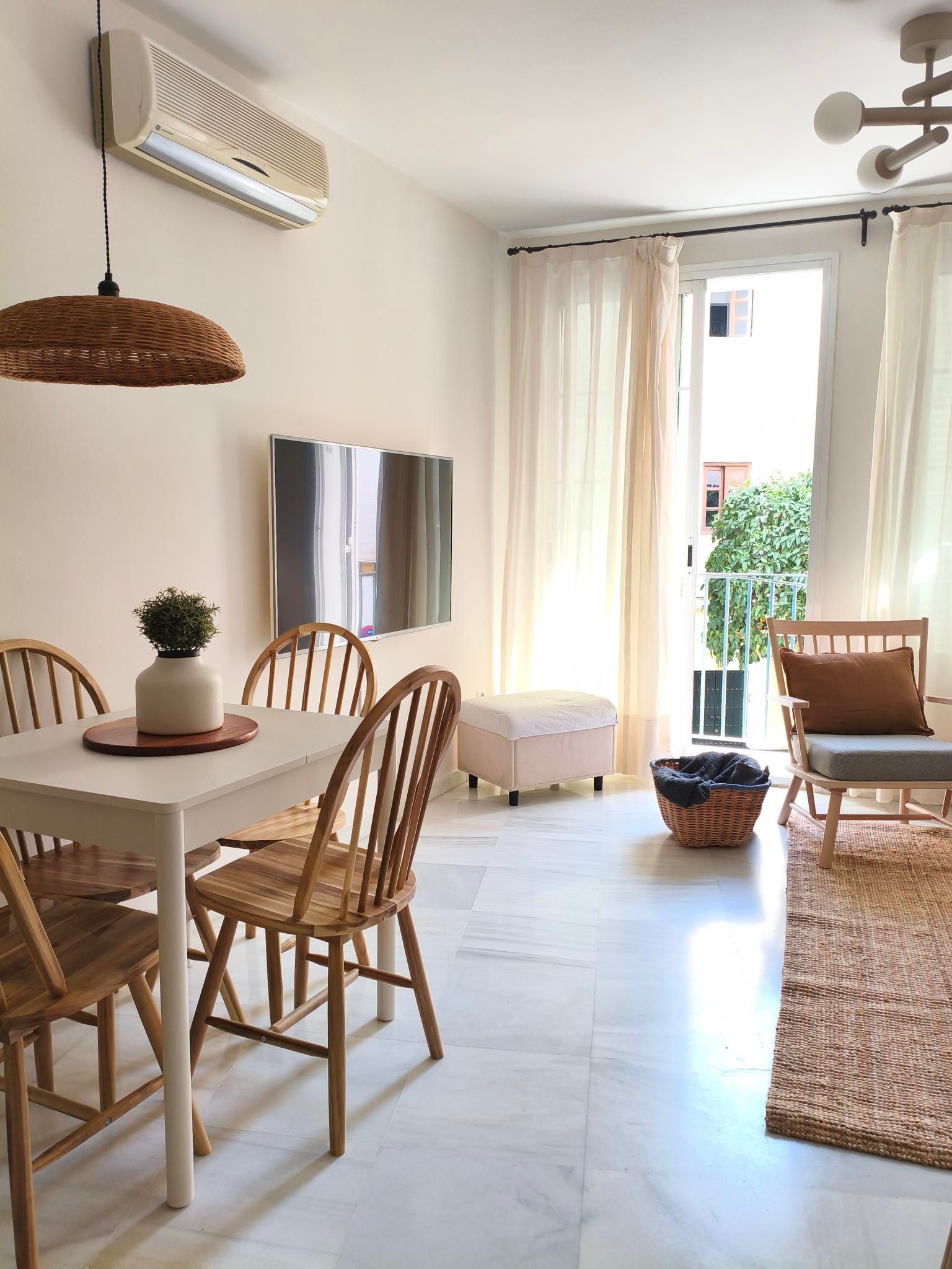 Dining area with a white table, wicker chairs, and a hanging woven light fixture.