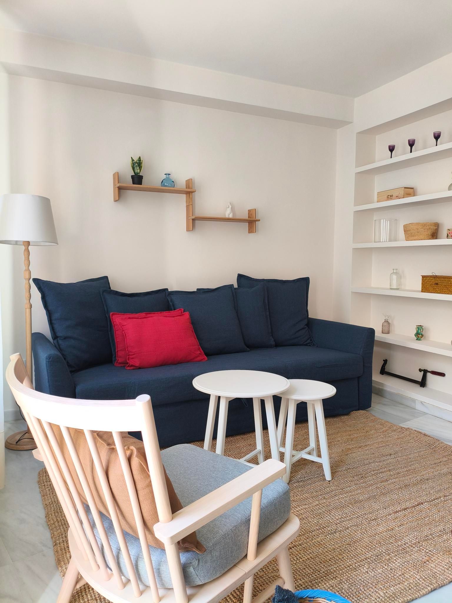 Living room with blue sofa, red pillow, wooden chair, small white tables, and built-in white shelves.