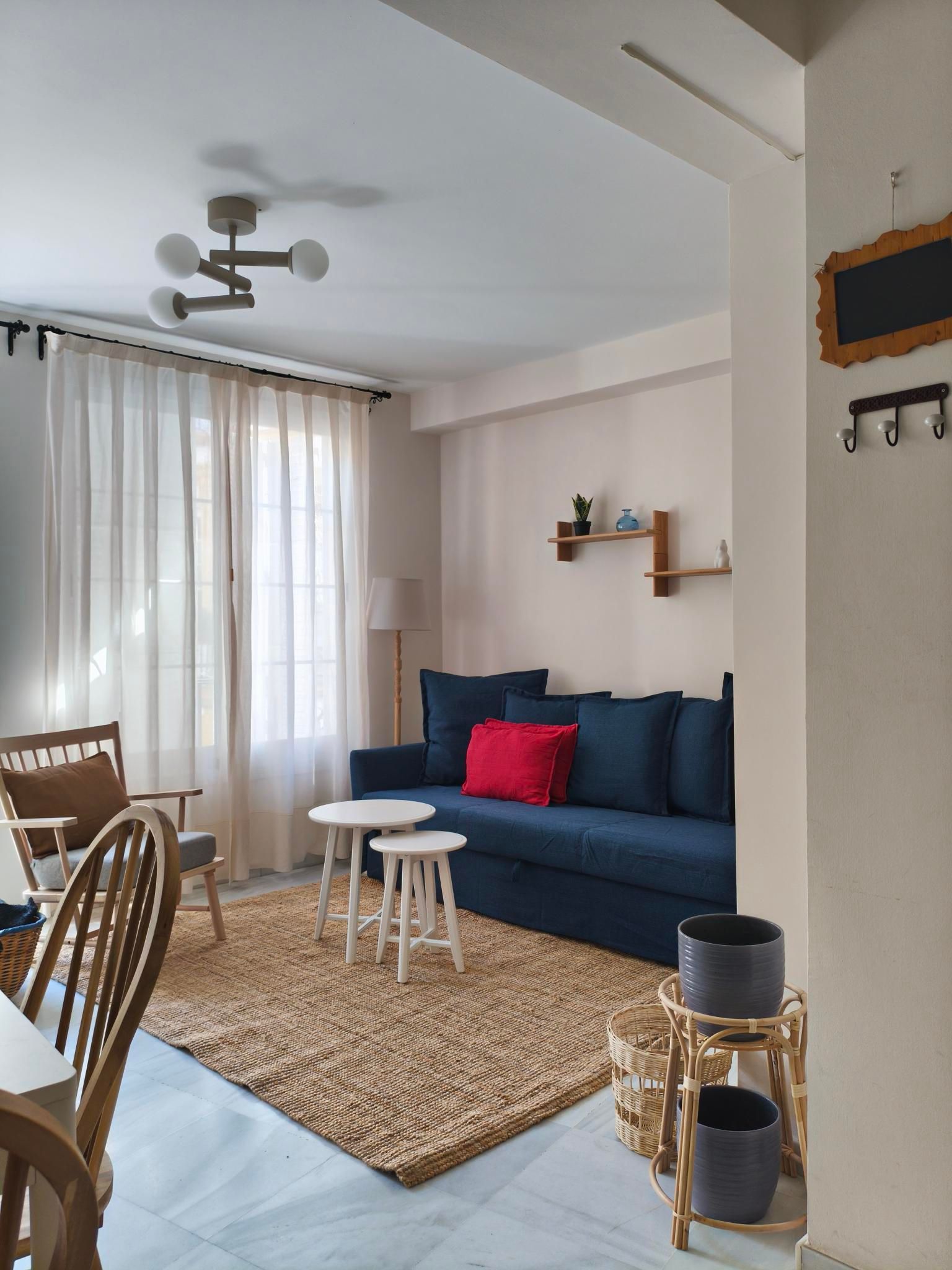 Living room with blue sofa, white curtains, wooden chair, and jute rug.