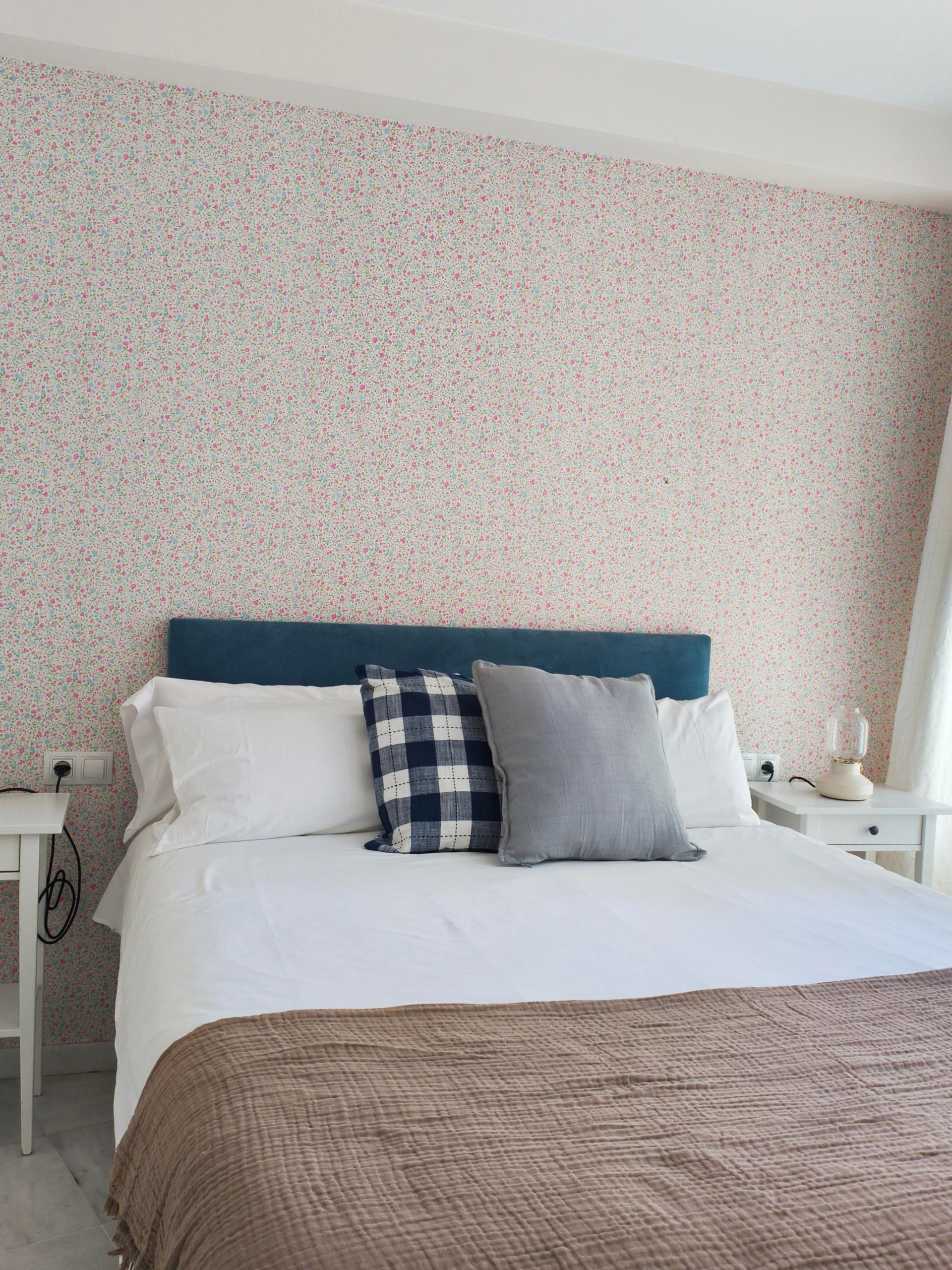 Bedroom with a bed, blue headboard, patterned wallpaper, and white bedside tables.