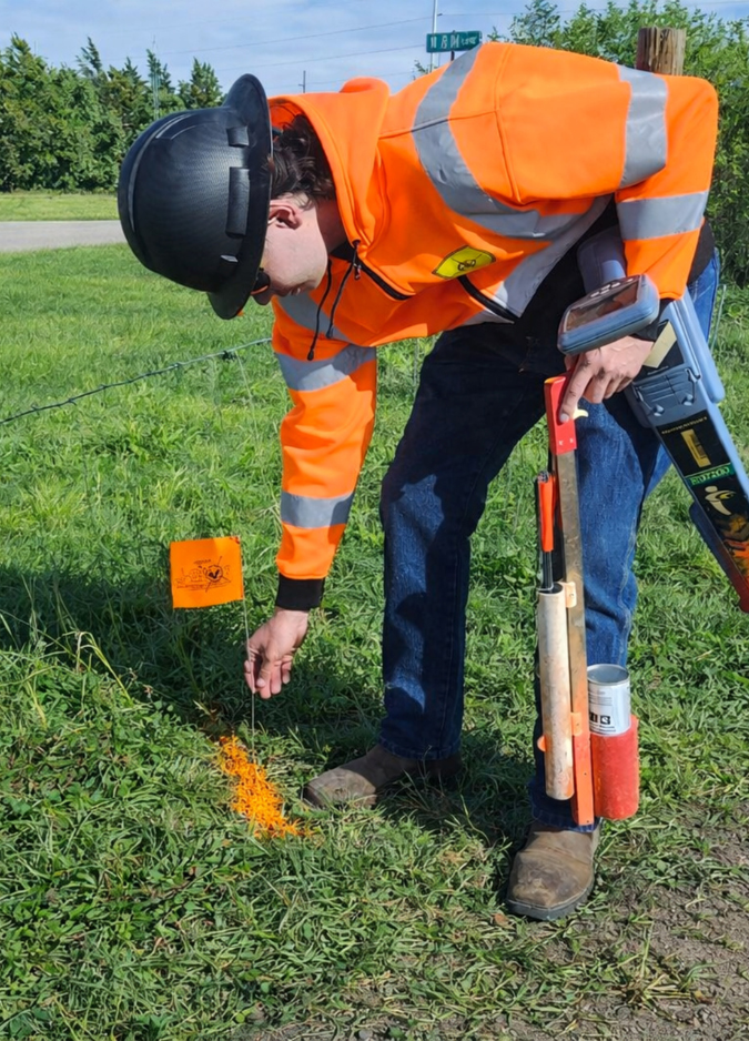 An orange utility warning flag for OPTK Networks marks buried fiber optic cables on a dirt lot.