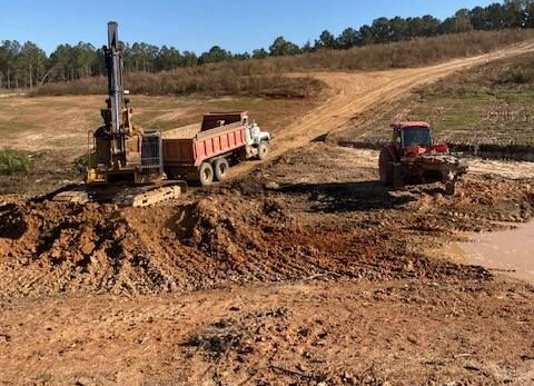 Construction site with an excavator, dump truck, and compactor working on dirt road under a blue sky.