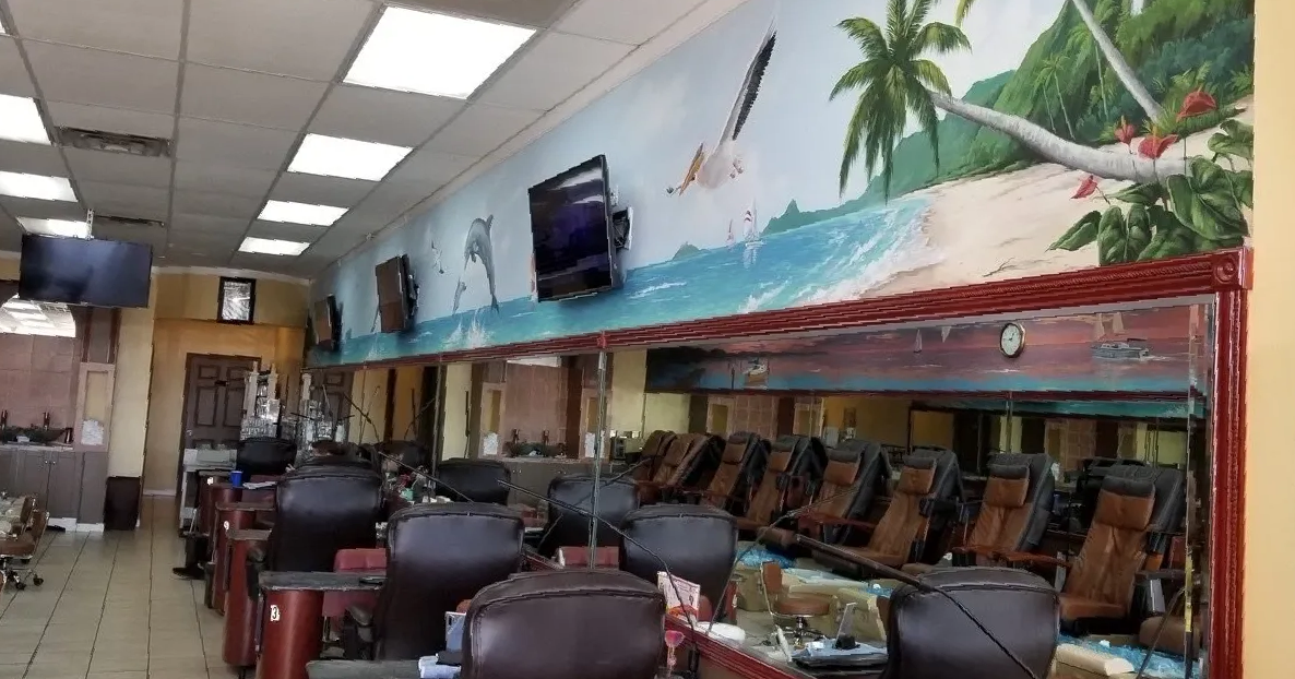 Six manicure tables along the right wall and a mirror running the full width of the salon.