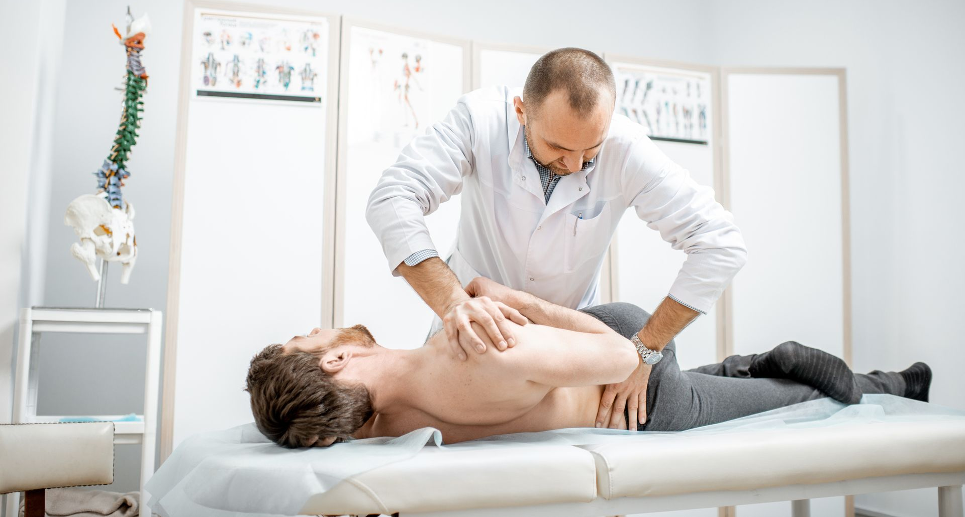 Chiropractor adjusting patient's spine on a white examination table in a bright room.