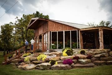 Rustic wooden house with large windows, stone steps, and colorful flowers in a landscaped garden.