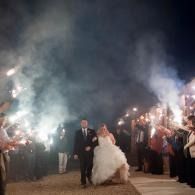 Bride and groom walk through a sparkler-lit nighttime wedding send-off as guests cheer on both sides