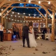 Bride and groom dancing in a rustic barn under string lights at a wedding reception