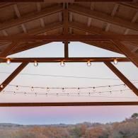 Wooden pavilion roof framing string lights over a hazy sunset landscape