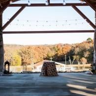 Open-air pavilion with a fire pit and string lights overlooking a wooded landscape