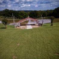 Small red-roofed pavilion beside a pond in a grassy park under a cloudy sky