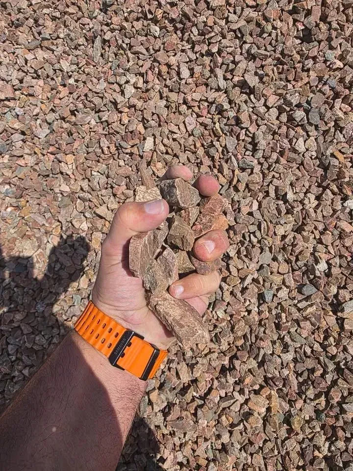 Hand holding brown gravel, orange wristband visible.