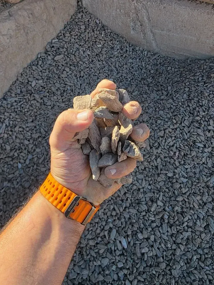 Handful of gray gravel with orange watch, outdoors on more gravel.