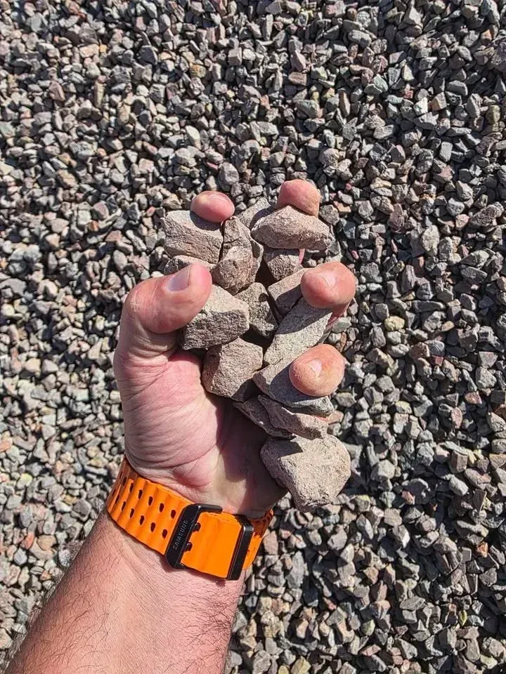 Hand holding a pile of gravel, with a bright orange watch.