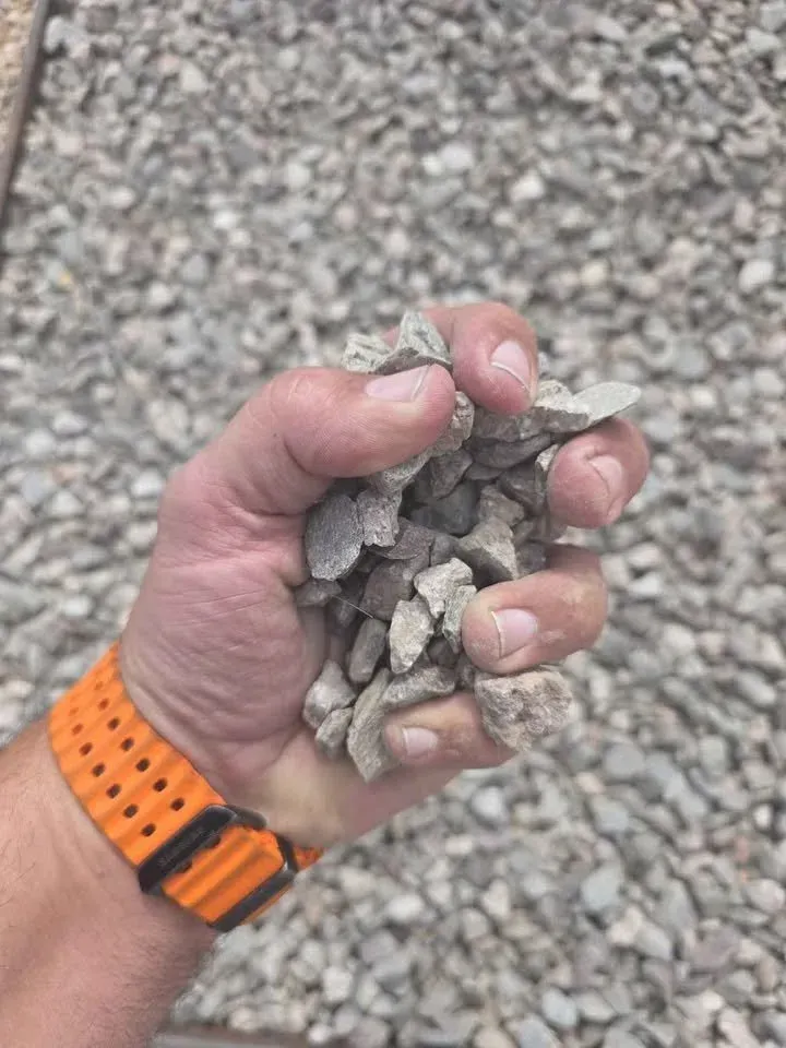 Handful of gray gravel, held by a person with an orange watch.