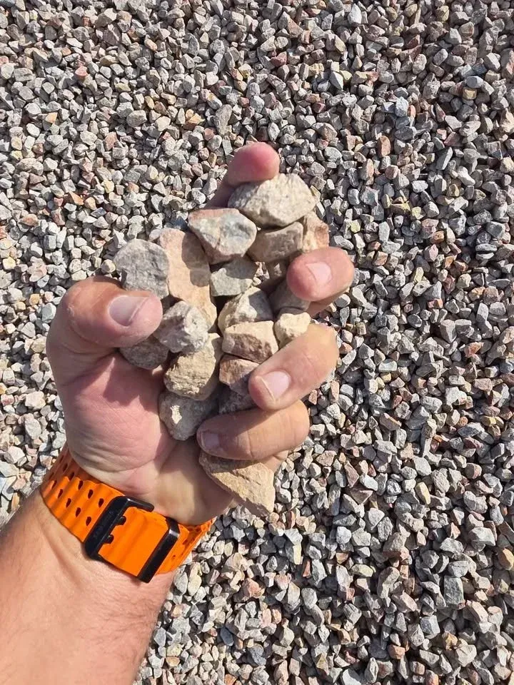 Hand holding a pile of light-colored gravel, arm with orange watch. Gravel background.