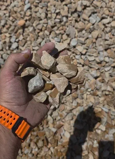 Hand holding a pile of beige and tan rocks; wrist with orange watch strap visible.