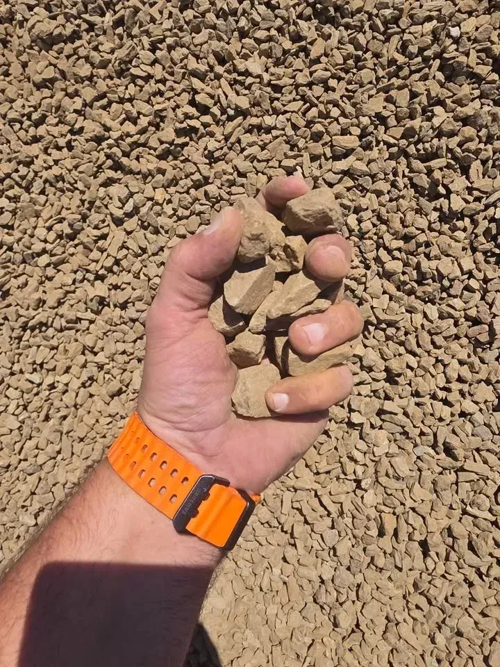 Handful of light brown gravel. Arm with orange watch.