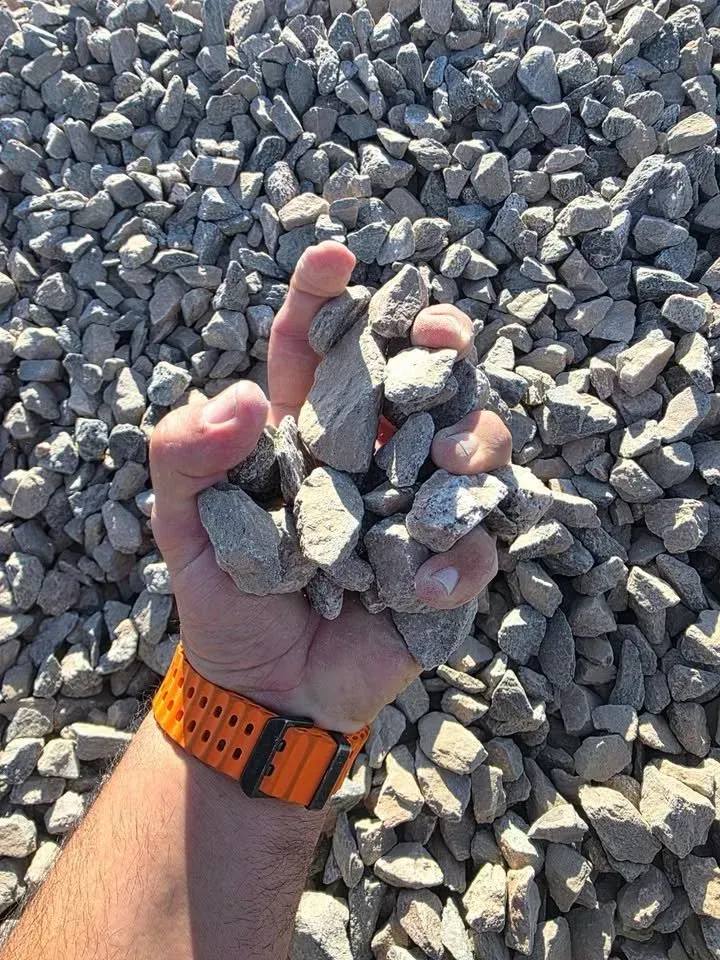 Handful of gray gravel held over a pile of similar stones; orange watch band visible.