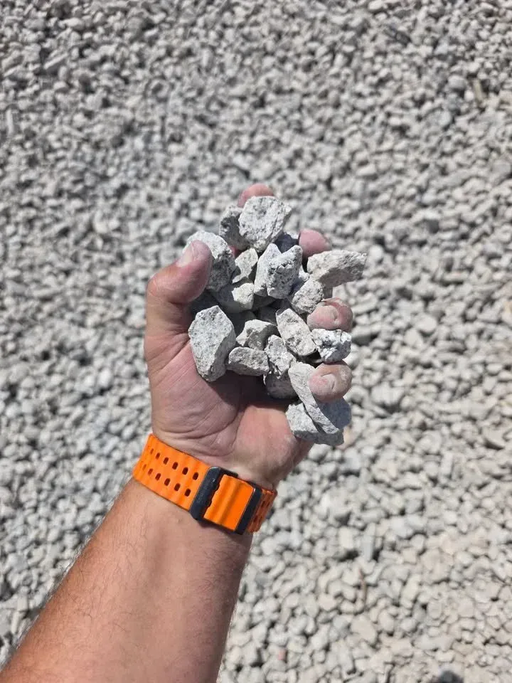 Handful of light-colored gravel. Arm with orange watch. Background is a pile of similar gravel.