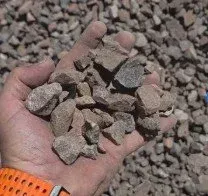 Hand holding small, light brown gravel stones, with more gravel in the background.