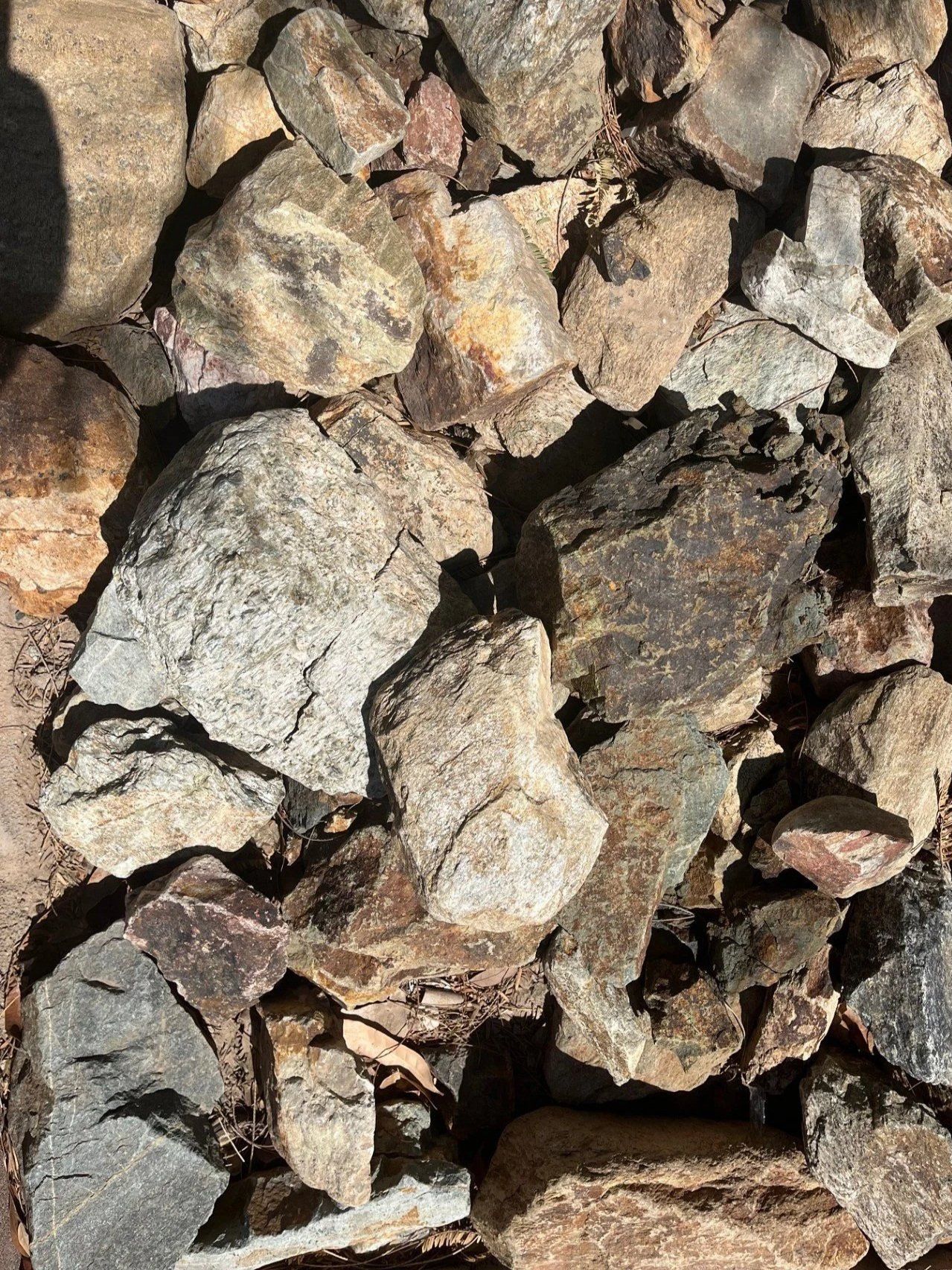 Pile of various sized rocks, mostly brown and grey, in sunlight.
