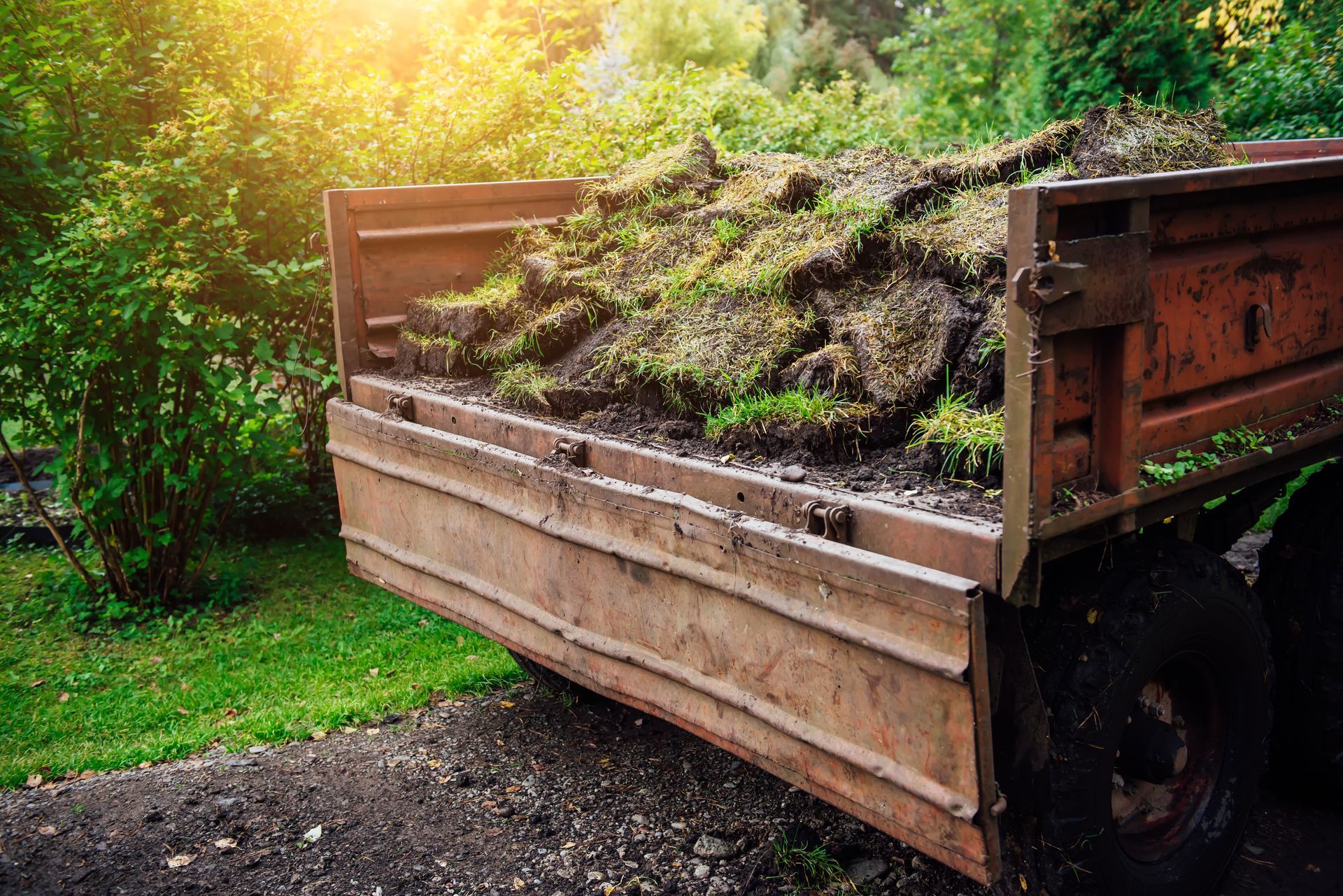 Truck bed filled with sod and dirt, parked on a gravel path near a green lawn.