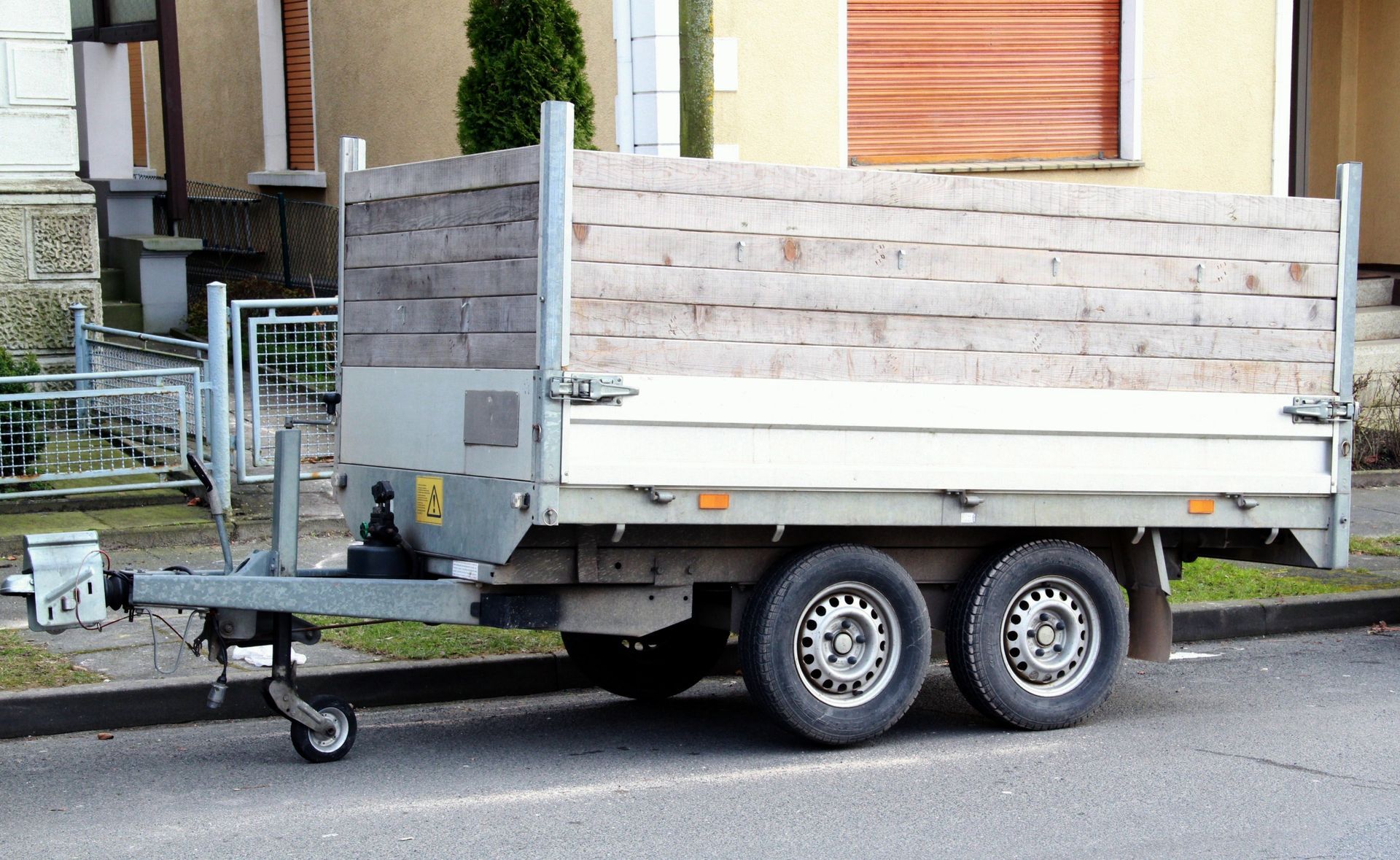 Trailer with wooden sides, parked on a street. Two tires, hitch, and metal frame.